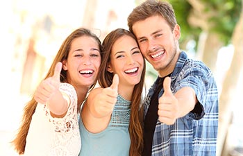 Two teenage girls and a teenage boy with perfect smiles showing their thumbs up.