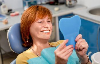 A satisfied senior woman in a dental chair looking at her perfect teeth in a mirror.