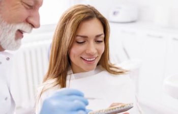 Dentist explaining porcelain veneers to a woman in a dental chair.