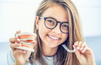 A young woman holding a dental model with traditional braces in one hand and a clear aligner in the other hand.