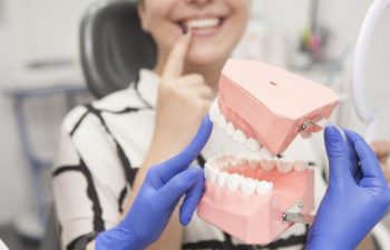 A dentist with a dental model explaining teeth restoration options to a woman sitting in a dental chair.