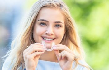 A beautiful young woman with a perfect smile holding a clear aligner for upper teeth.