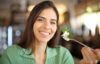 Happy woman holding fork with lettuce in a restaurant looking at camera